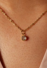 Gouden ketting met een schakeldesign, met een ronde hanger met een heldere, gefacetteerde steen in een gepolijste gouden zetting.
