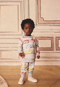 Hellgrauer Trainingsanzug mit Auto-Mustern in Rot, Blau, Grün und Gelb. Der Stoff hat eine weiche Textur; die Hosen sind an den Knöcheln mit Bündchen versehen.