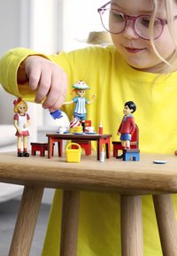 Kleurige speelgoedfiguren interageren rond een kleine houten tafel, met een gele mand, miniatuurservies en een gestructureerd houten oppervlak.