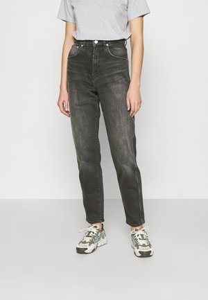 Mustat korkeat farkut suoran lahkeen kanssa, joissa on etutaskut, takataskut ja hienovarainen kivipesuefekti, yhdistettynä harmaaseen t-paitaan ja lenkkareihin.