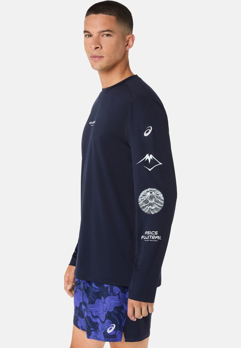 Haut de sport manches longues bleu marine avec logo et accents graphiques sur les manches, assorti à un short bleu arborant un motif ondulé.