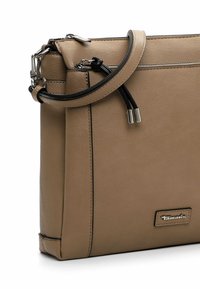 Braune Leder-Umhängetasche mit silbernem Reißverschluss, schwarzen Kordelzügen und silbernem Tamaris-Logo auf der Vorderseite.