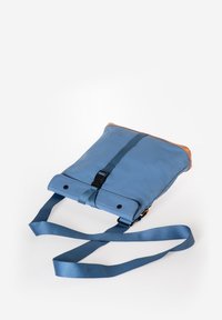 Borsa a tracolla blu con una texture liscia, dettagli in pelle color cuoio, chiusura magnetica e tracolla regolabile. Presenta un dettaglio con logo sulla parte anteriore.