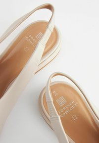 Beige slingback-kengät, jotka on valmistettu pehmeästä nahasta. Niissä on pyöreä kärki, valmistushypistelyllä varustettu elastinen nauha ja pehmustettu sisäpohja, jossa on brändäys.