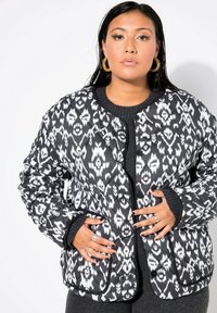 Giacca trapuntata a motivi in bianco e nero con collo rotondo, bottoni a pressione, polsini elastici e tasche laterali. Tessuto testurizzato con un design geometrico.