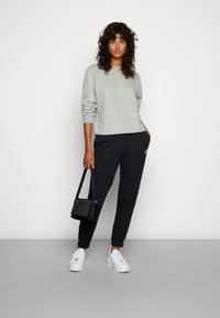Un ensemble avec un pull gris et un pantalon de survêtement noir. Le pull a des manches longues et le pantalon dispose de poches latérales; associé à des baskets blanches et un petit sac noir.