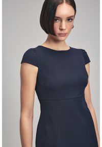 Vestido ajustado azul marino con mangas cortas abullonadas, escote redondo y costura en la cintura. Tejido liso y texturizado. Sin patrones visibles.
