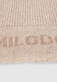 Beige strikket accessory med en ribbet tekstur og et subtilt præget logo i en lysere nuance. Materialet virker blødt og varmt.