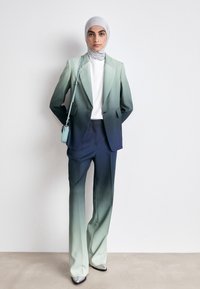 Ombre-Anzug mit grünem bis marineblauem Farbverlauf, taillierter Blazer und passenden Hosen; kombiniert mit einem weißen Oberteil und einer kleinen teal Handtasche. Silberschuhe.