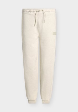 Pantalon de jogging en polaire beige avec taille élastique et cordon, jambes fuselées avec poignets aux chevilles, et petit logo rectangulaire sur la cuisse droite.
