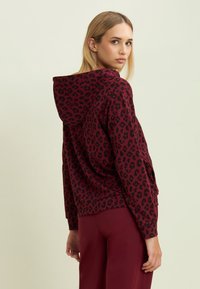 Sudadera color burdeos con estampado de leopardo negro, con capucha ajustable y puños de canalé. Combinada con pantalones burdeos a juego.