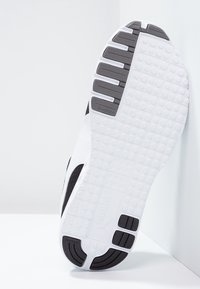 Semelle de chaussure de sport noire et blanche avec un caoutchouc текстuré, présentant un motif de sculpture, un logo de marque et un talon renforcé.