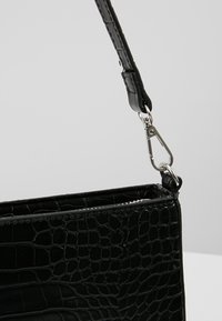Svart handväska i krokodilprägling med en strukturerad yta, utrustad med en avtagbar rem och metallklämma för stängning.