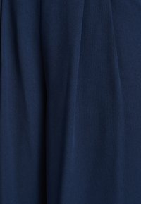 Tamnoplava tkanina s glatkom teksturom i mekim padajem; karakteriziraju je istaknuti nabori, što ukazuje na naborani dizajn.