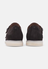 Chaussures en daim marron foncé à profil bas, dotées d'une semelle en caoutchouc blanche et d'accents à boucle réglable sur les côtés.
