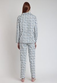 Conjunto de pijama de franela en gris claro con patrón de corazones azul marino. Incluye mangas largas, cuello y pantalones a juego con cintura elástica.