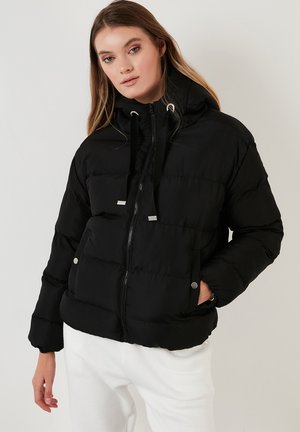 Black puffer jacket with a zip-up front, adjustable drawstring hood, horizontal stitching, and silver hardware accents. Soft fabric texture.