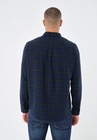 Camicia a scacchi blu navy con accenti verdi, maniche lunghe, colletto abbottonato e orlo curvo. Tessuto morbido con finitura texture.