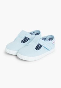 Zapatos de lona azul claro con suelas de goma blancas, aberturas recortadas y un forro de cuadro vichy azul marino. Presentan tiras elásticas para facilitar su uso.