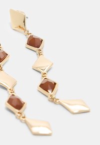 Ohrringe mit goldfarbigem Tropfen haben geometrische Formen mit braunen facettierten Steinen. Das Design umfasst diamant- und rechteckige Akzente, die visuelles Interesse erzeugen.