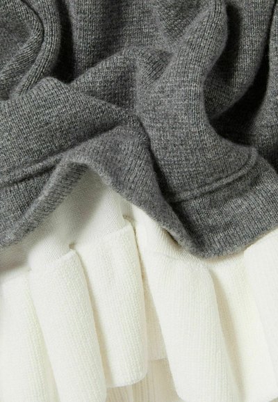 Tela de punto gris superpuesta sobre una tela blanca con canalé estructurado, creando un contraste suave y texturizado con pliegues y bordes visibles.