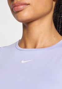 Lila sporttanktop van gladde stof, met een ronde halslijn en een wit Nike-logo op de borst.