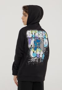 Felpa nera in cotone, con una grafica colorata in stile graffiti sulla schiena, che include testo e un'illustrazione di un controller per giochi.