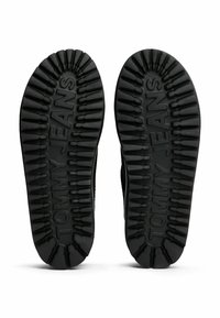 Suelas de zapatos de goma negra con patrones de relieve pronunciados y el logotipo grabado "TOMMY JEANS", que ofrecen agarre y durabilidad.