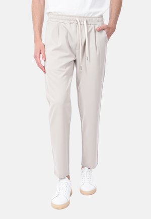 Pantaloni beige chiaro con elastico in vita e cordino, dotati di tasche laterali, realizzati in un tessuto morbido, abbinati a sneakers bianche.