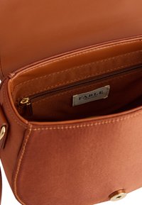 Brown leather crossbody bag with a smooth texture, featuring a zipper pocket and a gold-tone snap closure. Inner brand label visible.