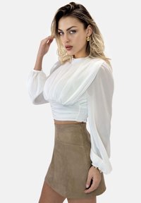 Hvid bluse med voluminøse ærmer og elastisk talje, kombineret med en beige ruskindsmininederdel. Tilbehør inkluderer guldbøjler.