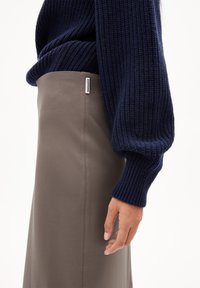 Un pull en maille côtelée marine associé à une jupe en cuir taupe lisse, mettant en valeur une silhouette élégante et des textures contrastées.