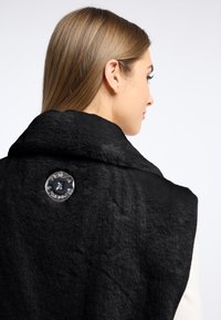 Czarna kamizelka z sztucznego futra z szerokim kołnierzem, z błyszczącym detalem w postaci guzika z tyłu. Tekstura jest miękka i puszysta, co nadaje ciepły wygląd.