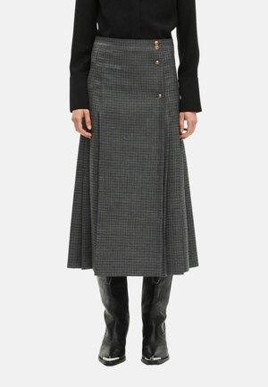 Jupe midi à carreaux gris avec un design évasé, ornée de trois boutons dorés sur le côté et d'un tissu texturé. Portée avec des bottes de cowboy noires.
