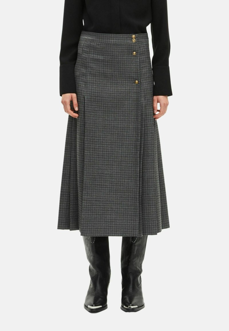Jupe midi à carreaux gris avec un design évasé, ornée de trois boutons dorés sur le côté et d'un tissu texturé. Portée avec des bottes de cowboy noires.