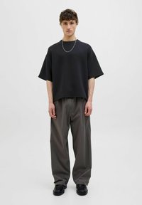 Sort oversized kortærmet T-shirt parret med grå brede bukser og sorte chunky sko; enkelt design, glat tekstur.