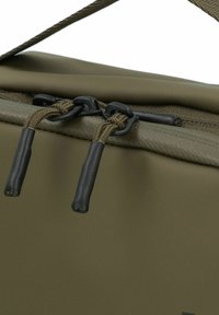 Bolsa aislante de color verde oliva con un acabado suave y mate que presenta herrajes negros, cremallera expuesta y asas de tirón robustas y texturizadas.