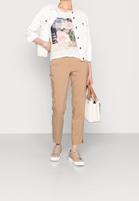 White denim jacket, graphic t-shirt with floral print, tan fitted pants, and beige sneakers. White handbag with brown accents.