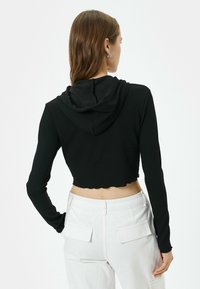 Hoodie recortado negro de canalé con mangas largas y dobladillo festoneado. Cuenta con una capucha y una textura suave, combinado con pantalones baggy blancos.