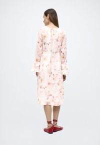 Φλοράλ midi φόρεμα σε ανοιχτό ροζ ύφασμα, με μακριά μανίκια και ρεβέρ με βολάν. Διαθέτει δέσιμο στη μέση και άνετη εφαρμογή. Κόκκινα φλατ παπούτσια.