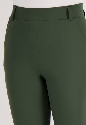 Donkergroene broek van een gladde, rekbare stof. Bevat een hoge taille, voorzakken en een aansluitend ontwerp. Minimale stikseldetails.