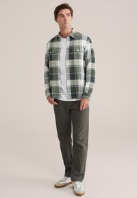 Zeleni i bijeli karirani flanel košulja s dvjema prsnim džepovima, nosi se preko bijelog T-shirta, u kombinaciji s tamnim hlačama i ležernim tenisicama.