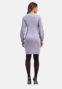 Graues, geripptes Strickkleid mit langen Ärmeln, figurbetontem Schnitt und geradem Saum, kombiniert mit schwarzen Strumpfhosen und hochhackigen Schuhen.