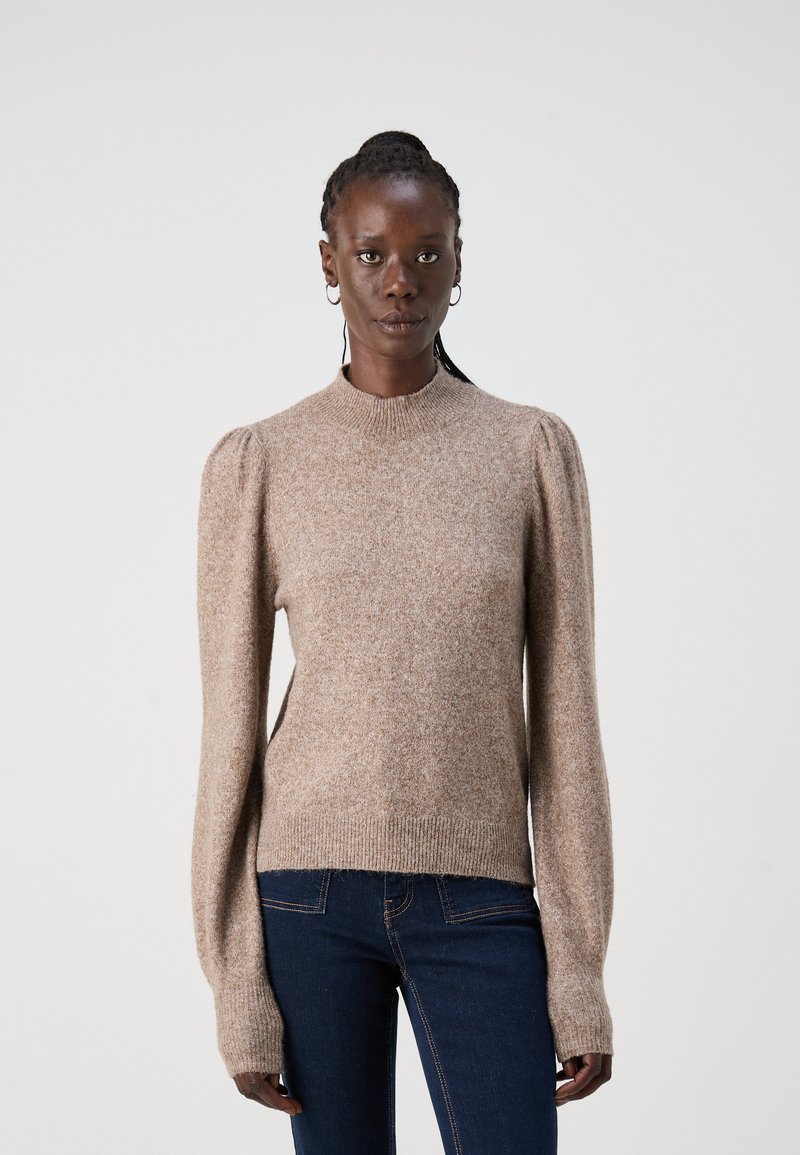 Beige ullgenser med rund hals, puffede ermer og ribbestrikkede mansjetter. Glatt tekstur med et subtilt melert mønster. Figursydd silhuett.