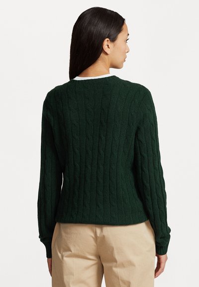 Pull en maille torsadée vert foncé, à manches longues, avec un col rond et un motif texturé. Tissu doux avec un ourlet côtelé, associé à un pantalon neutre.
