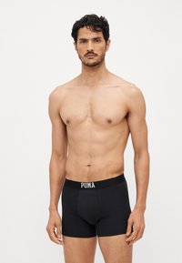 Fekete boxer alsónadrág, puha pamutból készült, testhezálló kialakítással. Jellemzője a márkás derékpánt, fehér betűkkel "PUMA" felirattal.