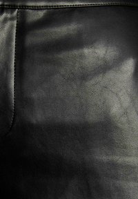 Superficie in pelle nera che mostra una trama texturizzata, con un dettaglio di cucitura sul lato sinistro e sottili variazioni di tonalità su tutto il materiale.