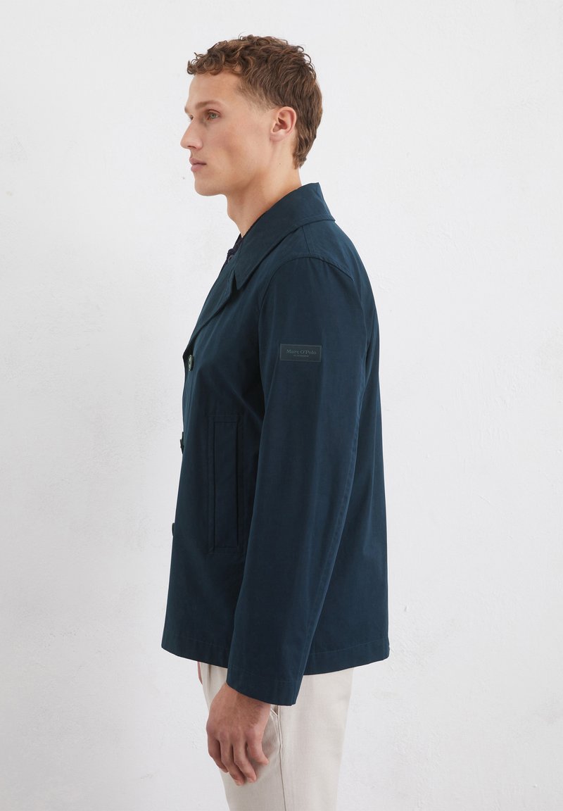 Marineblaue leichte Jacke mit Reverskragen, Knöpfen vorne, zwei seitlichen Taschen und einem Logodetail am linken Ärmel.