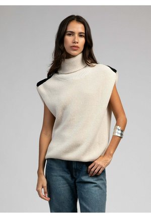 Top sans manches en tricot crème avec un col montant et des accents noirs sur les épaules, associé à un jean en denim bleu. Présente une coupe décontractée et un tissu texturé.