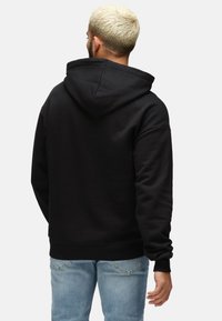 Sudadera negra con capucha y cordones, de textura suave y puños de canalé. Lleva puesta encima de unos vaqueros de un azul claro. Diseño simple y casual.
